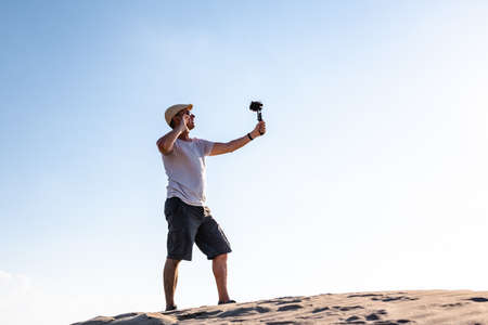 Side view of male traveler standing on sand dune and filming content for social mediaの写真素材