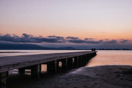 Anonymous persons sitting on pier near sea at sunsetの写真素材