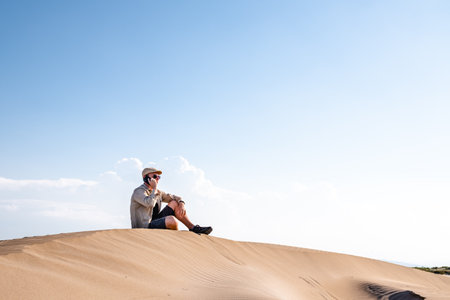 Man calling with a smart phone sitting in the desert dunes alone. Copy spaceの写真素材