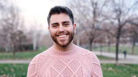 Man looking at the camera and smiling while standing outdoors in the park.