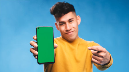 Man pointing to a mobile phone with green screen while standing on an isolated background.