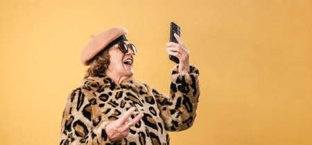 Stylish senior woman using her mobile phone while standing on an isolated background.の写真素材