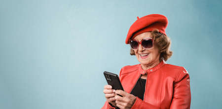 Stylish senior woman smiling while using her mobile phone over an isolated background.の写真素材