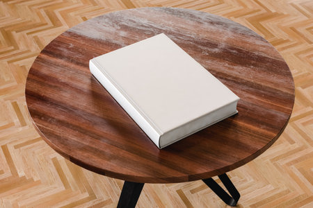 From above of white mock up book placed on round wooden table in light living room with laminate in...