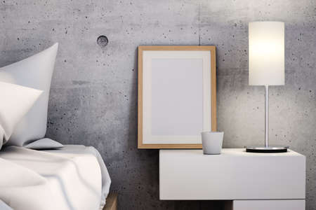 Vertical empty frame and glowing lamp placed on bedside table near bed against concrete wall in modern bedroom. 3d renderingの写真素材