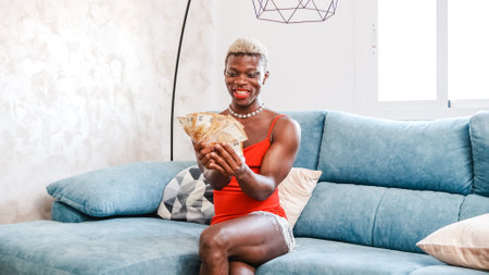 Excited African American person in stylish red dress with makeup examining bunch of moneyの写真素材