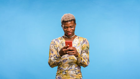 African androgynous person texting on cellphone on blue backgroundの写真素材