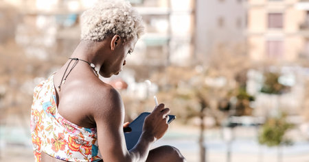 African transgender woman sitting on stairs, listening to audio on her phoneの写真素材