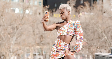 Trendy black queer person in dress taking selfie on streetの写真素材