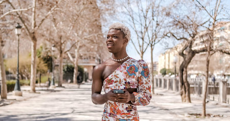 Stylish transgender person smiling while using a mobile phone walking outdoors.