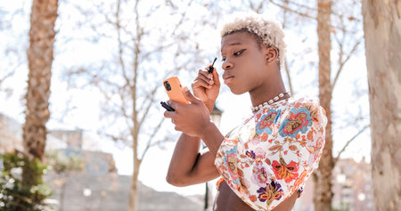 Focused black transgender person applying mascara on streetの写真素材