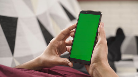 Person holding a mobile phone with a green screen, ready to replace it with any contentの写真素材