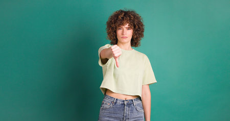 Adult woman with curly hair looking unhappy showing thumbs down gestureの写真素材