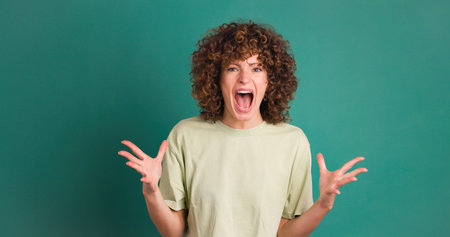 Shocked young woman showing stretched hands with palms on green background