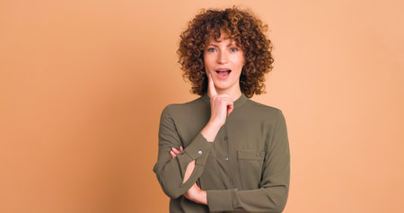 Thoughtful young woman touching face and smiling on beige backgroundの写真素材