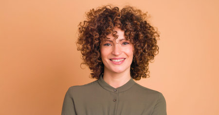 Smiling standing young curly haired woman on beige background