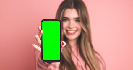 Female model showing smartphone with blank green screen over pink backgroundの写真素材
