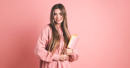 Happy female university student carrying backpack and holding books on pink