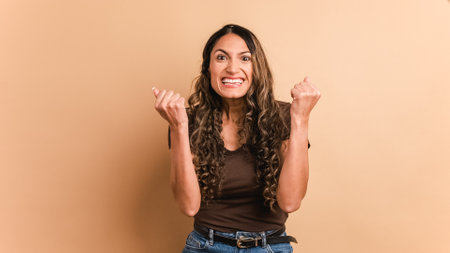 Happy hispanic woman celebrating raising fists and looking at cameraの写真素材