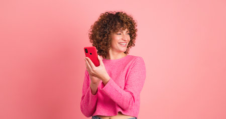 Cheerful woman taking selfie with smartphone in pink studioの写真素材