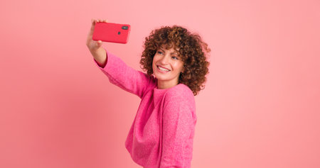 Cheerful woman taking self pictures with mobile phone on pink backgroundの写真素材