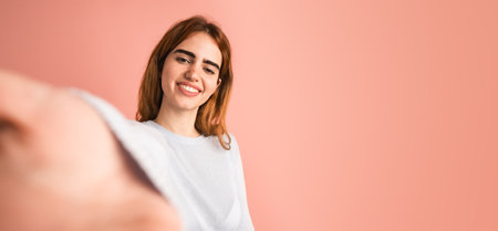 Smiling young woman taking selfie in pink studioの写真素材