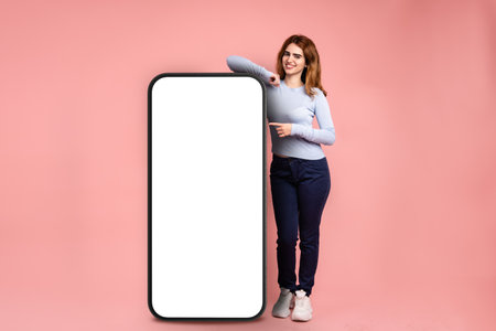 Happy woman pointing at cellphone with blank screen in studioの写真素材