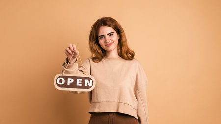 Happy woman holding open sign in brown studioの写真素材