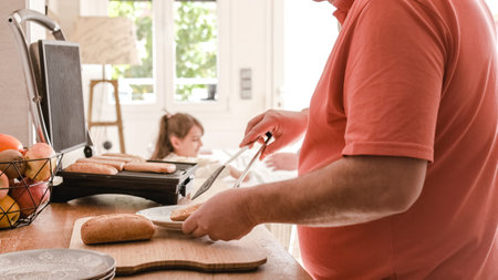 Man warming up bread in the kitchen while his granddaughter watches himの写真素材