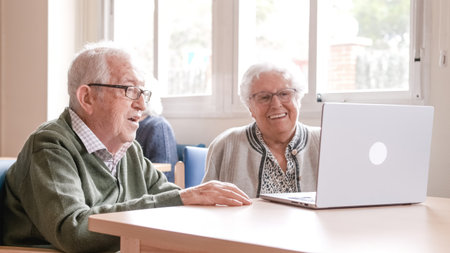 Happy senior couple chatting online using laptop at nursing homeの写真素材