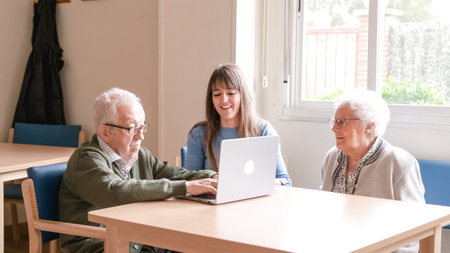 Happy granddaughter teaching senior people to use laptop at nursing homeの写真素材