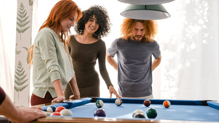 Happy friends looking at billiard balls on pool table in game room at home