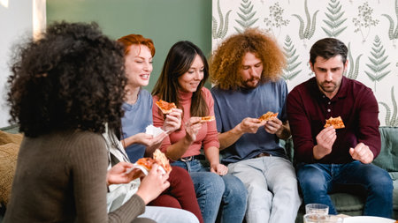 Happy friends enjoying pizza slices in living room during weekend partyの写真素材
