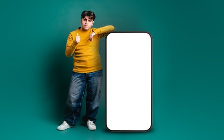 Smiling man showing thumbs up near huge cellphone with blank screenの写真素材