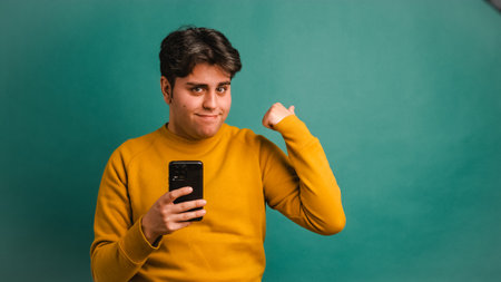 Smiling man with mobile phone pointing away in studioの写真素材