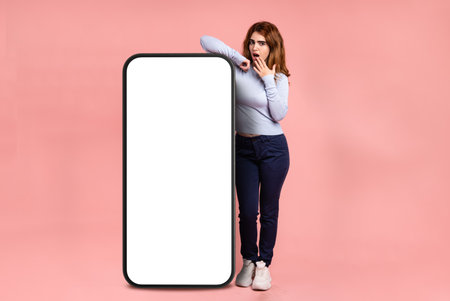 Amazed woman leaning on huge mobile phone with blank screenの写真素材