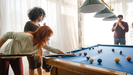 Woman aiming cue on billiard ball while playing pool with friends at home
