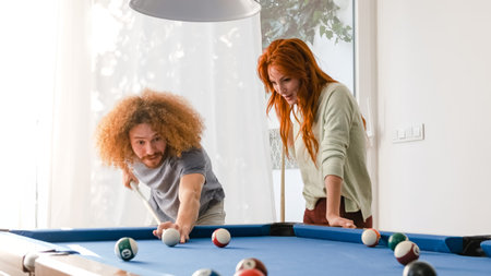 Man aiming cue stick on billiard ball while playing pool with woman at home