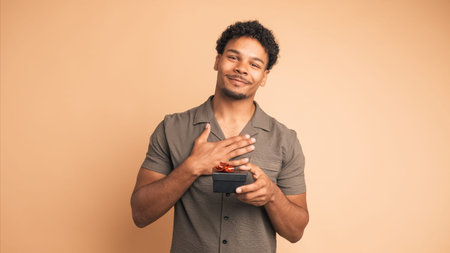 Happy young man receiving gift box in beige studio