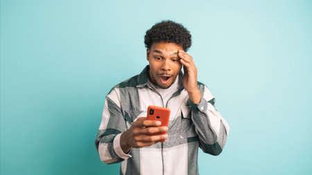 Cheerful young man using smartphone in blue studioの写真素材