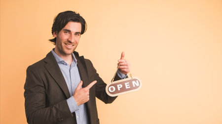 Smiling businessman with open sign inviting in brown studioの写真素材
