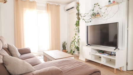 Sunlit living room with cozy sofa and large televisionの写真素材