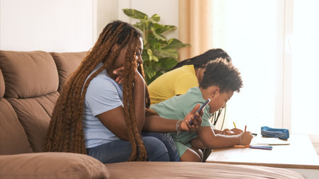 Mother using smartphone while daughter and son coloring in book at homeの写真素材