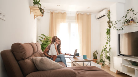 Girl with mother using netbook on sofa at homeの写真素材