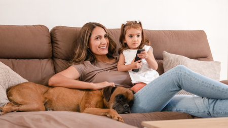 Happy family with cute dog watching TV on sofa at homeの写真素材