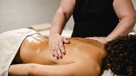 Masseuse applying oil on womans back during relaxing massage therapy sessionの写真素材