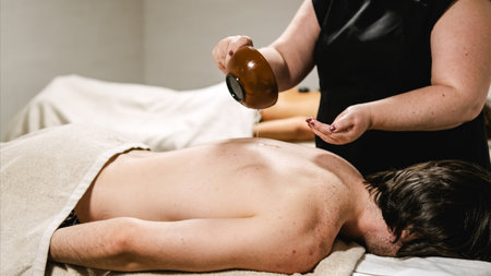 Masseur pouring oil on mans back during relaxing massage therapy sessionの写真素材