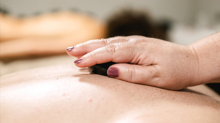 Massage therapist placing hot stone on clients back during spa treatmentの写真素材