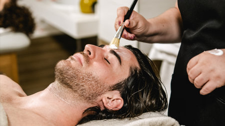 Beautician applying cosmetic mask on mans face in beauty salonの写真素材