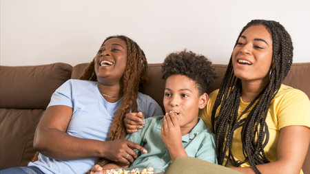 Cheerful family eating popcorns and enjoying while watching TV at homeの写真素材